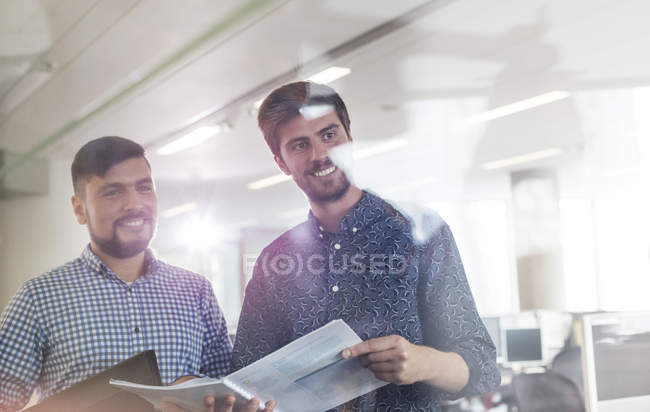 Hombres de negocios sonrientes revisando el papeleo en la oficina - foto de stock