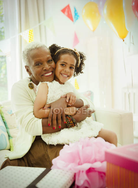 Retrato sonriente abuela y nieta abrazándose en fiesta de cumpleaños - foto de stock