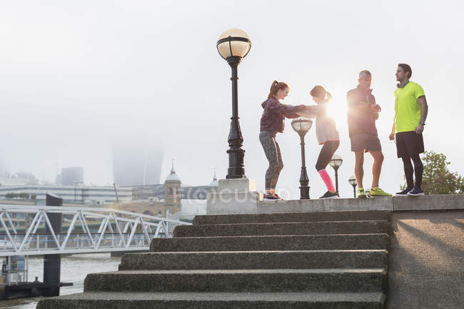 Runners stretching and talking at sunny urban waterfront — Stock Photo