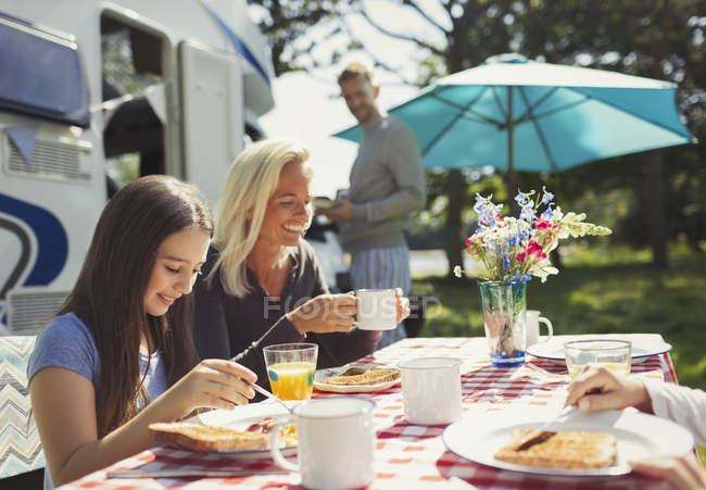 Lächelnde Mutter und Tochter genießen das Frühstück vor dem sonnigen Wohnmobil — Stockfoto