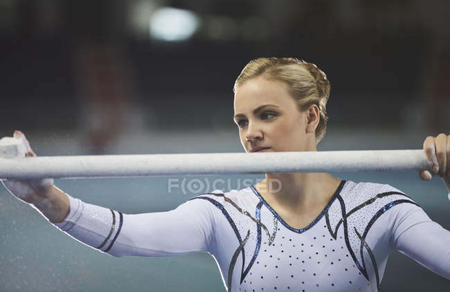 Female gymnast using chalk on uneven bars in arena — Stock Photo