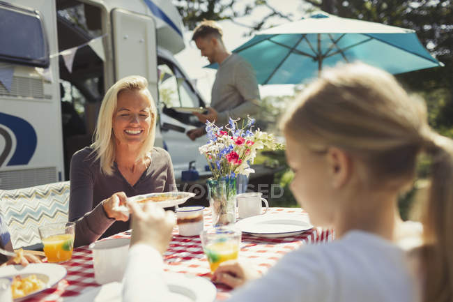 Lächelnde Mutter und Tochter genießen das Frühstück am Tisch vor dem sonnigen Wohnmobil — Stockfoto