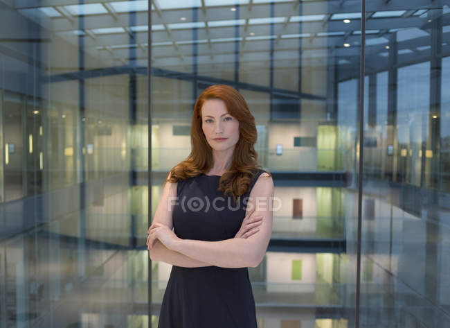 Retrato mujer de negocios confiada con el pelo rojo en el atrio de la oficina moderna - foto de stock