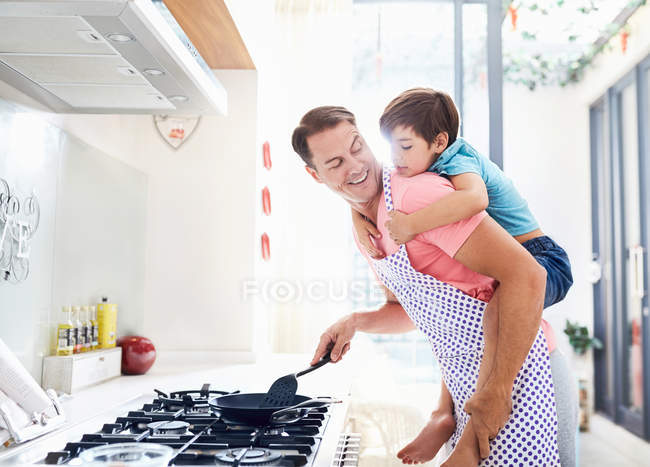 Father piggybacking son, cooking at stove in kitchen — Stock Photo