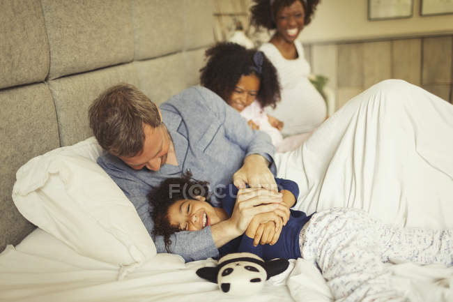 Multi-étnico pai e filha cócegas e rindo na cama — Fotografia de Stock