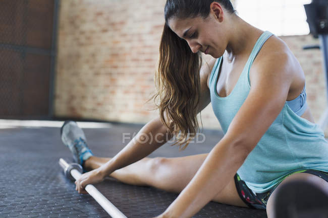 Focused young woman stretching leg, using barbell in gym — Stock Photo