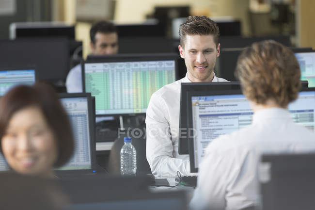 Empresarios trabajando en computadoras en oficina de planta abierta - foto de stock