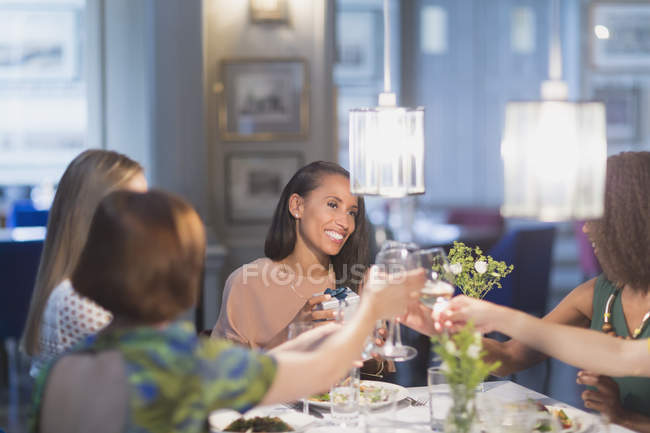 Mulheres sorridentes amigos brindar copos de vinho branco jantar na mesa do restaurante — Fotografia de Stock