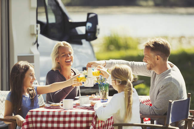 Familie prostet Kaffee und Orangensaftgläser am Tisch vor sonnigem Wohnmobil zu — Stockfoto