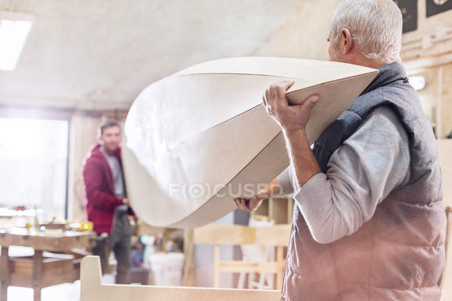 Carpinteiros masculinos carregando barco de madeira na oficina — Fotografia de Stock