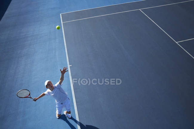 Vue aérienne jeune joueur de tennis masculin jouant au tennis, servant la balle sur un court de tennis bleu ensoleillé — Photo de stock