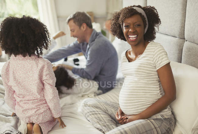 Portrait laughing pregnant woman with young family on bed — Stock Photo