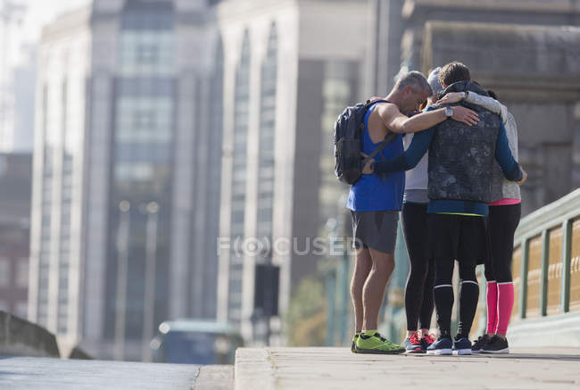 Runners connected in a huddle on sunny urban sidewalk — Stock Photo