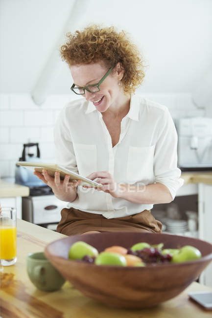 Retrato de mulher sentada e olhando para tablet digital na cozinha, sorrindo — Fotografia de Stock