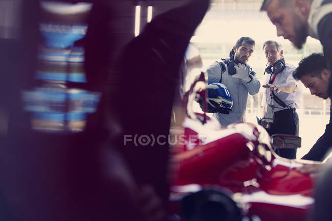 Gerente e fórmula um piloto de carro de corrida falando na garagem de reparação — Fotografia de Stock