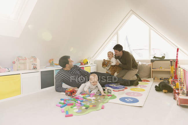 Male gay parents playing with baby sons in playroom — Stock Photo