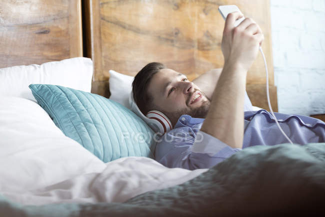 Чоловік слухає музику з навушниками та mp3 плеєром, що лежить на ліжку — стокове фото