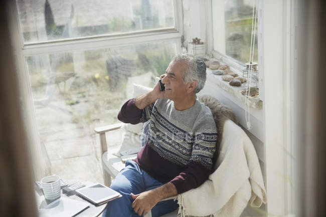 Старший чоловік розмовляє по мобільному телефону на сонячному ганку — стокове фото