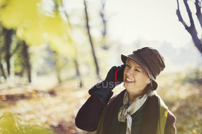 Старшая женщина разговаривает по мобильному телефону в солнечном осеннем парке — стоковое фото
