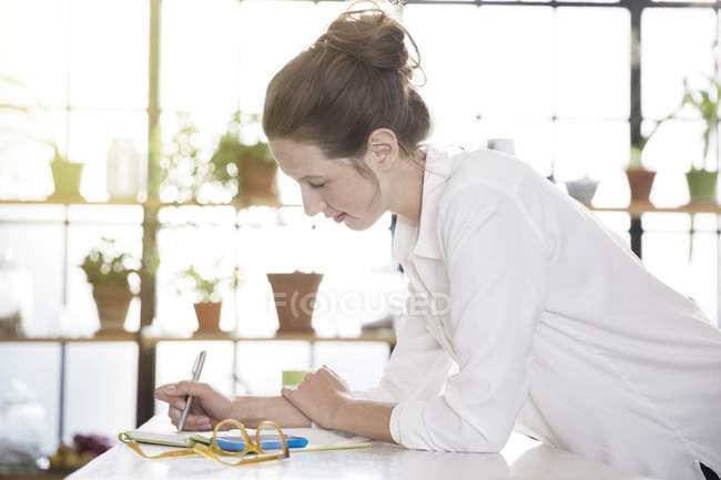 Mujer joven apoyada en el escritorio y la escritura - foto de stock