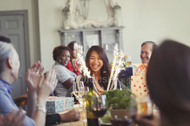 Amigos viendo feliz mujer con fuegos artificiales pastel de cumpleaños en la mesa del restaurante - foto de stock