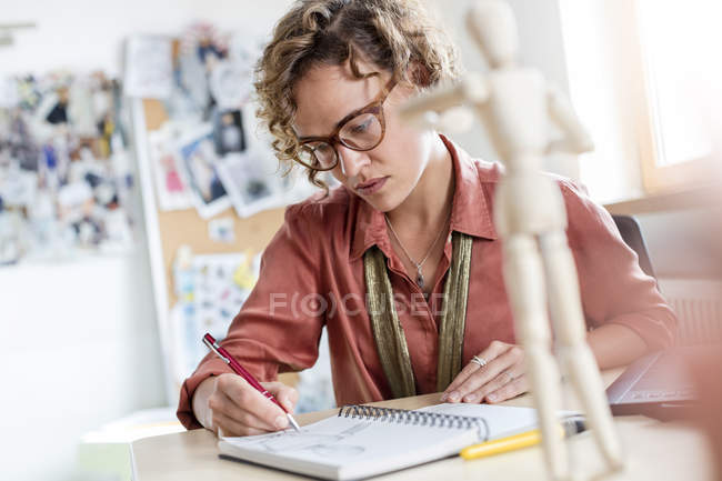 Croquis professionnel de design féminin ciblé dans un carnet de notes au bureau — Photo de stock