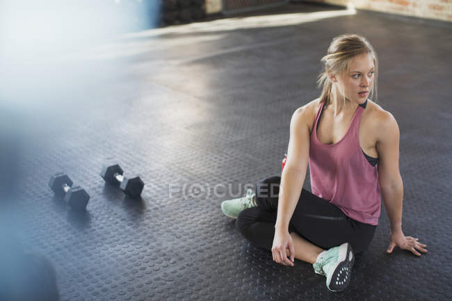 Молодая женщина растягивается, крутится в спортзале рядом с гантелями — стоковое фото