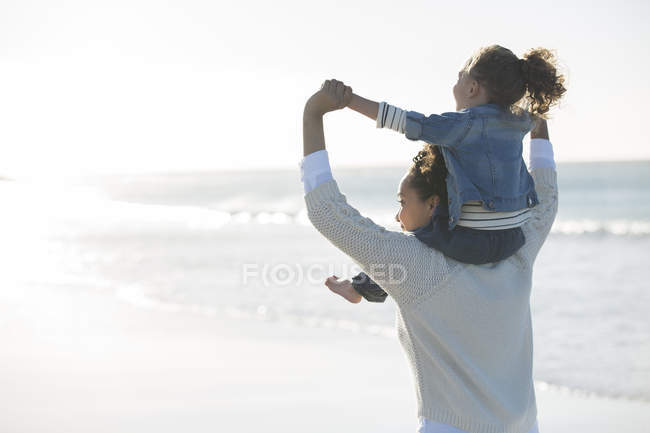 Madre cargando hija en sus hombros en la playa - foto de stock