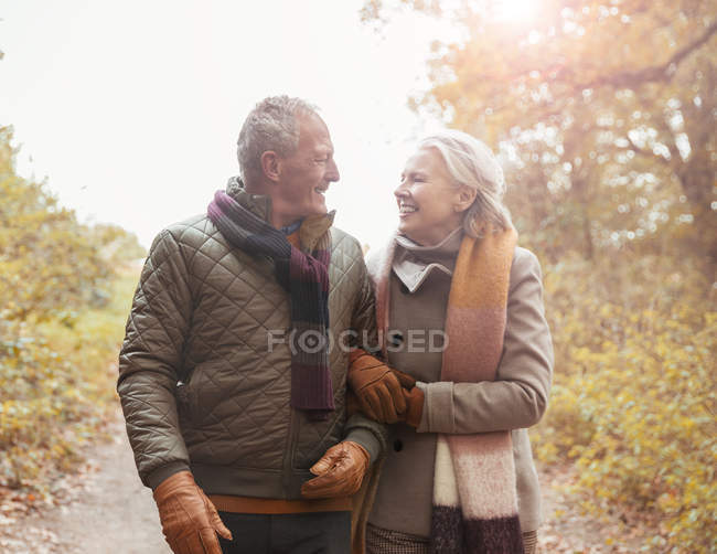 Ласковая пожилая пара, идущая рука об руку по дорожке в осеннем парке — стоковое фото
