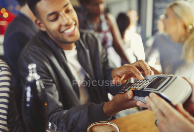 Homem sorridente pagando bartender usando leitor de cartão de crédito no bar — Fotografia de Stock
