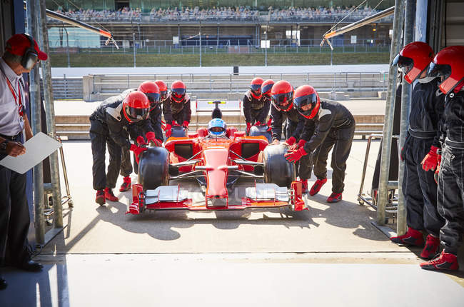 Pit tripulación empujando fórmula de un coche de carreras en el garaje de reparación - foto de stock