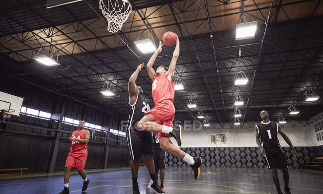 Young male basketball players playing basketball on court in gymnasium — Stock Photo