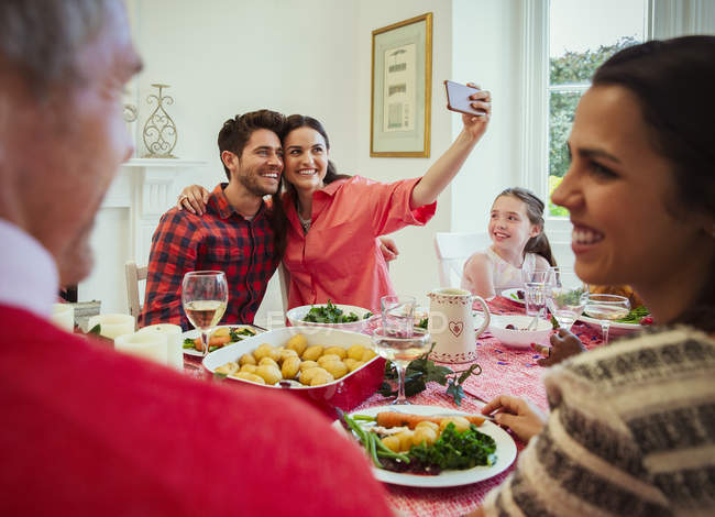 Pareja con teléfono de la cámara tomando selfie en la mesa de la cena de Navidad - foto de stock