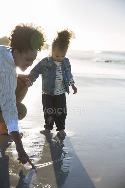 Mother and daughter drawing on wet sand on beach — Stock Photo