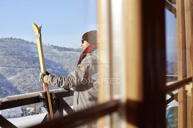 Male skier with skis on sunny cabin balcony — Stock Photo