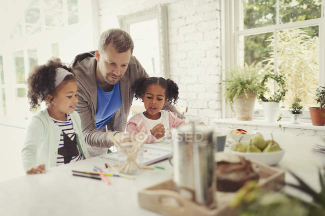 Multi-ethnic father and daughters coloring in kitchen — Stock Photo