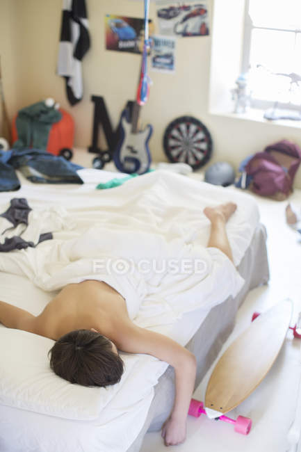 Adolescente durmiendo en la cama en su habitación desordenada - foto de stock