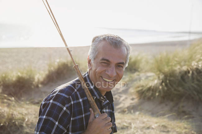 Ritratto uomo anziano sorridente con canna da pesca che cammina sulla spiaggia soleggiata — Foto stock