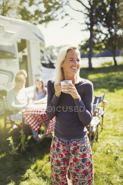 Donna sorridente in pigiama bere caffè fuori solare camper — Foto stock