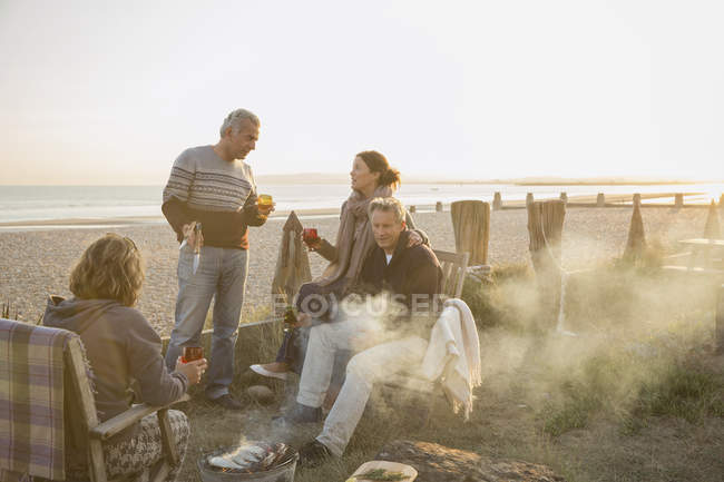 Couples matures buvant du vin et barbecuant sur la plage du coucher du soleil — Photo de stock