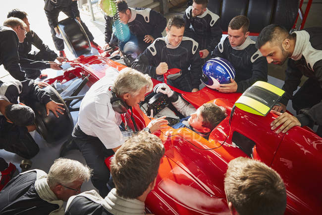 Gerente y equipo de boxes rodeando a un piloto de fórmula en un coche de carreras - foto de stock
