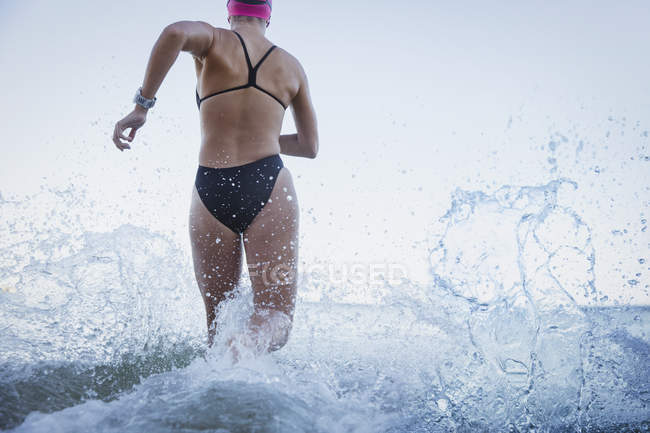 Mujer nadadora de aguas abiertas corriendo y salpicando en el océano surf - foto de stock