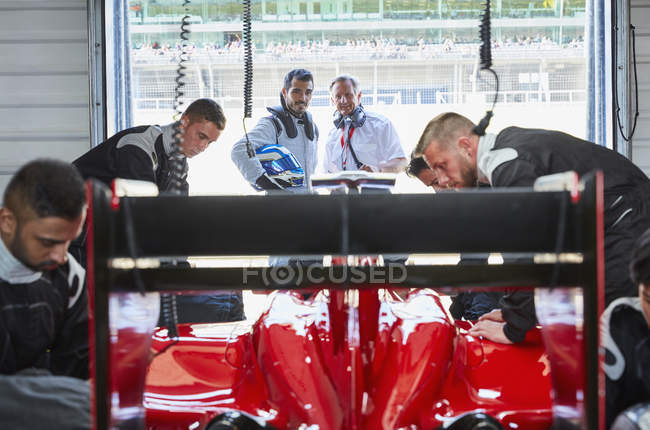 Equipo de hoyo trabajando en la fórmula de un coche de carreras en el garaje de reparación - foto de stock