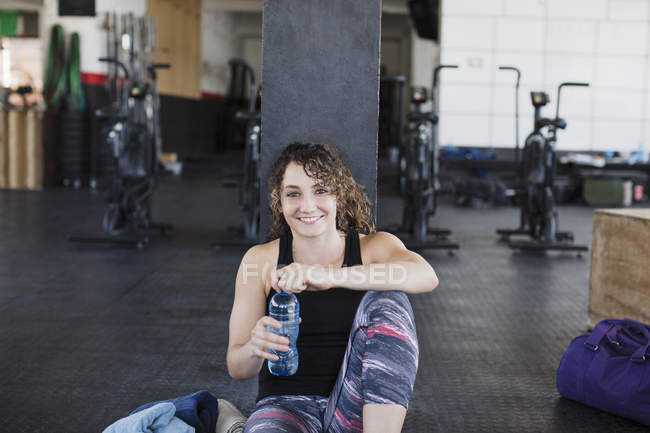 Portrait smiling, confident young woman drinking water and resting post workout in gym — Stock Photo