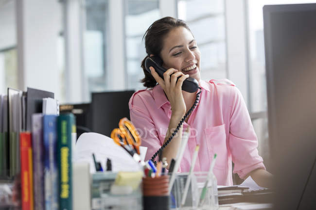 Femme d'affaires souriante parlant au téléphone travaillant à l'ordinateur dans le bureau — Photo de stock