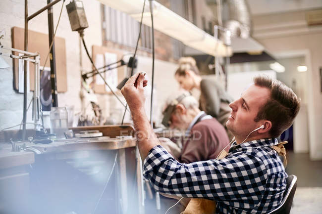 Male jeweler listening to music with headphones working in workshop — Stock Photo