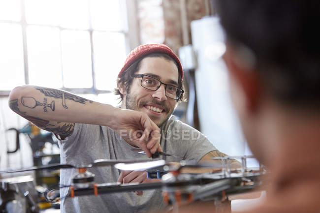 Diseñador masculino sonriente con tatuajes ensamblando drones - foto de stock