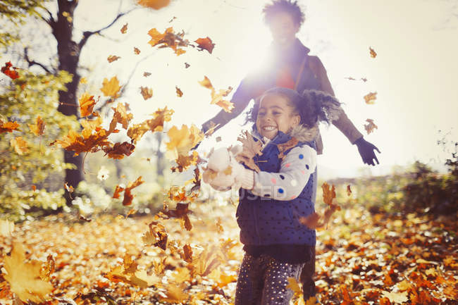 Madre giocosa e figlia gettando foglie autunnali nel parco soleggiato — Foto stock