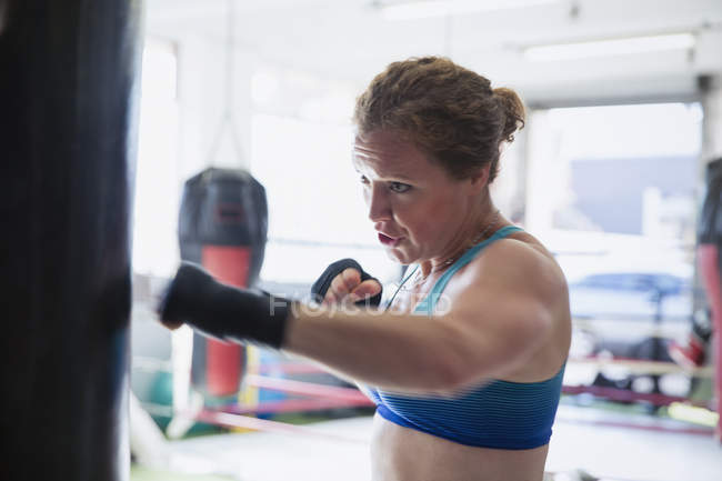 Determinado boxe boxer feminino no saco de perfuração no ginásio — Fotografia de Stock