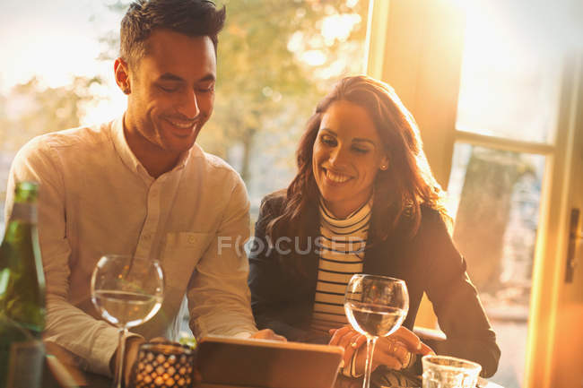 Casal jovem bebendo vinho e usando tablet digital no restaurante ensolarado — Fotografia de Stock